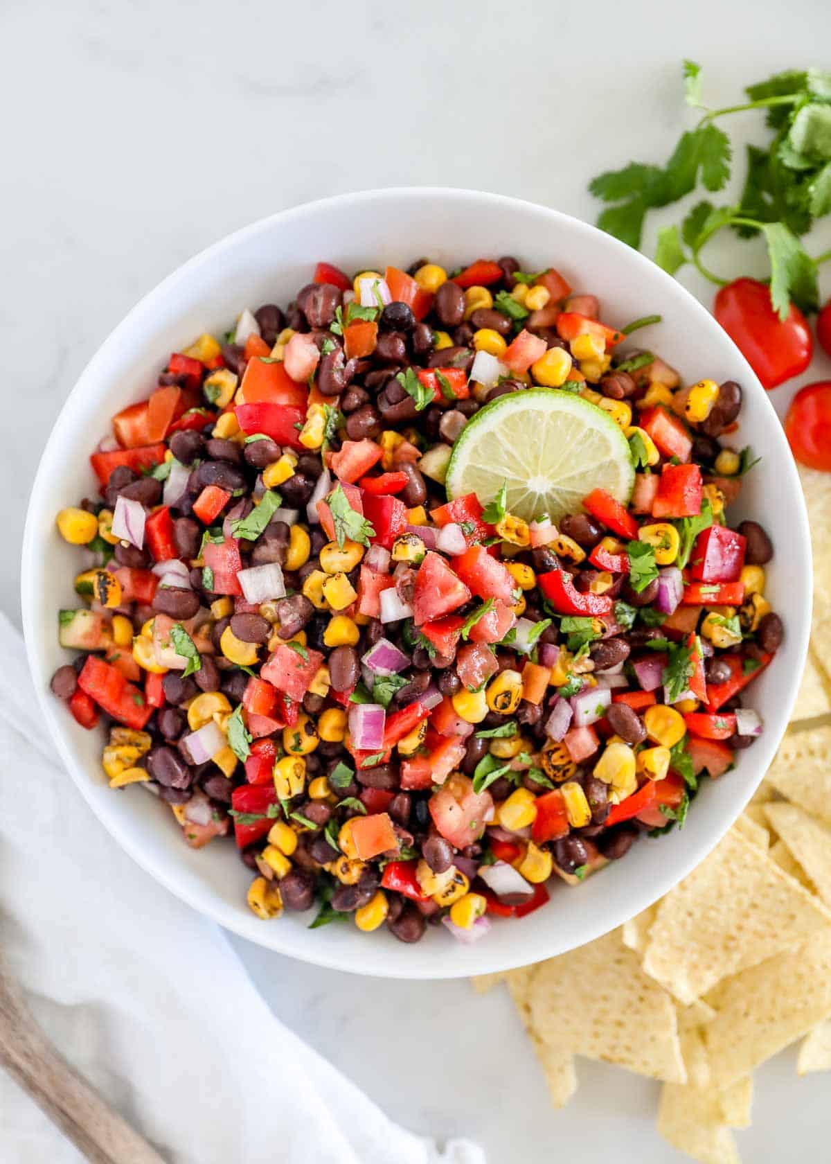 Fresh and colorful black bean salsa is easy to make with canned beans and simple, flavorful ingredients. It's a crowd-pleaser at parties, picnics or anytime you need a snack. Black bean salsa in a white bowl with chips on the side for dipping.