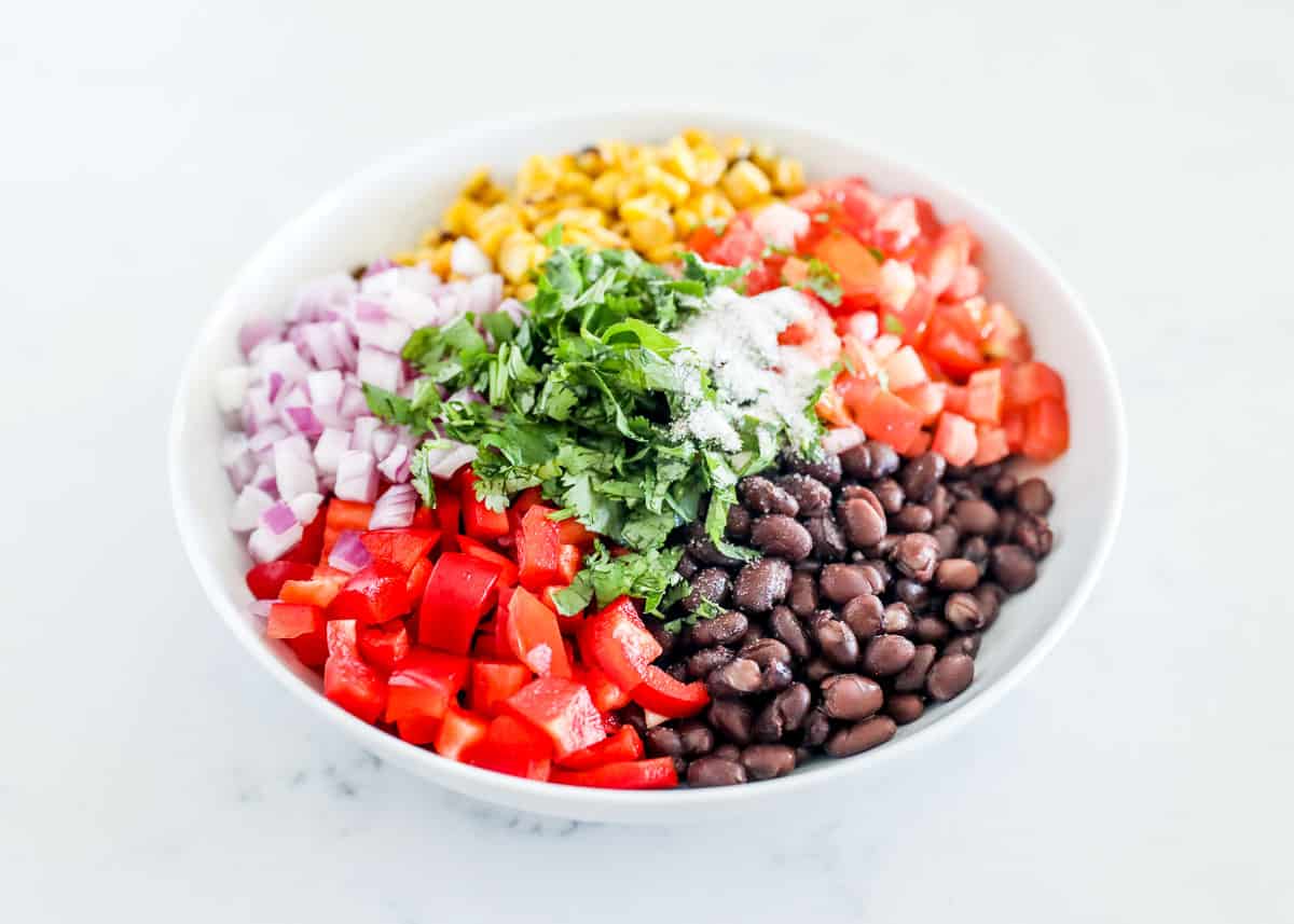 Tomatoes, red pepper, tomatoes, corn, red onion, cilantro and black beans in a bowl.
