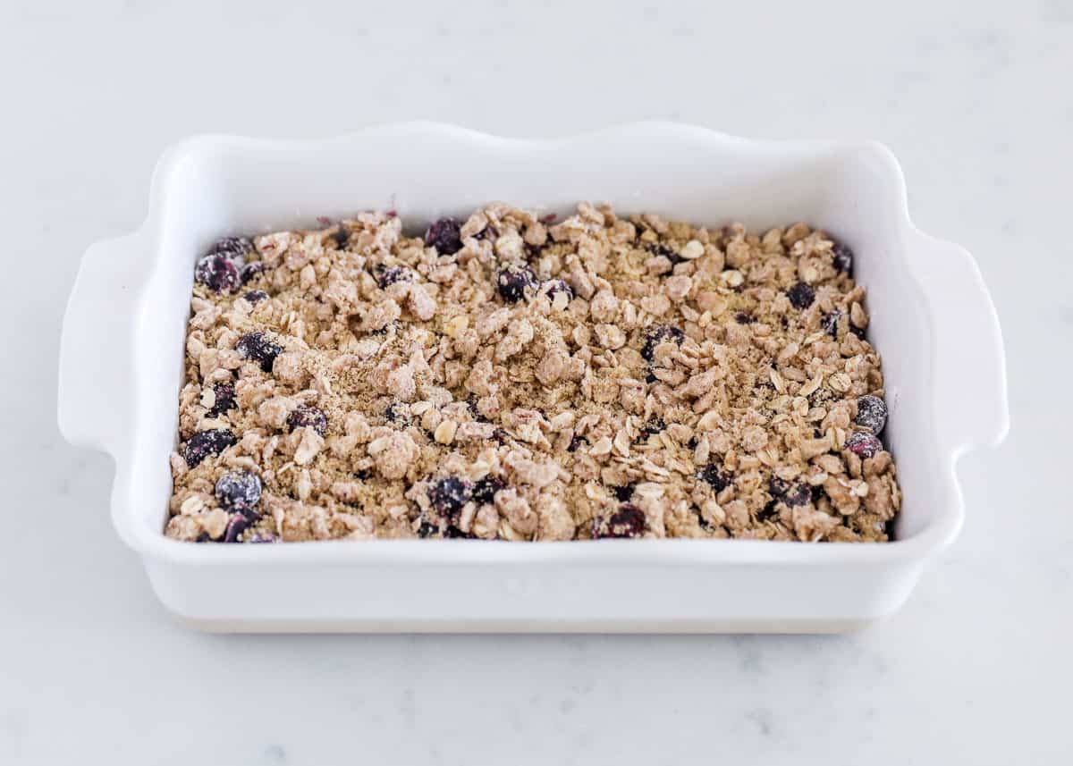 Unbaked blueberry crisp in a white baking dish with streusel on top.