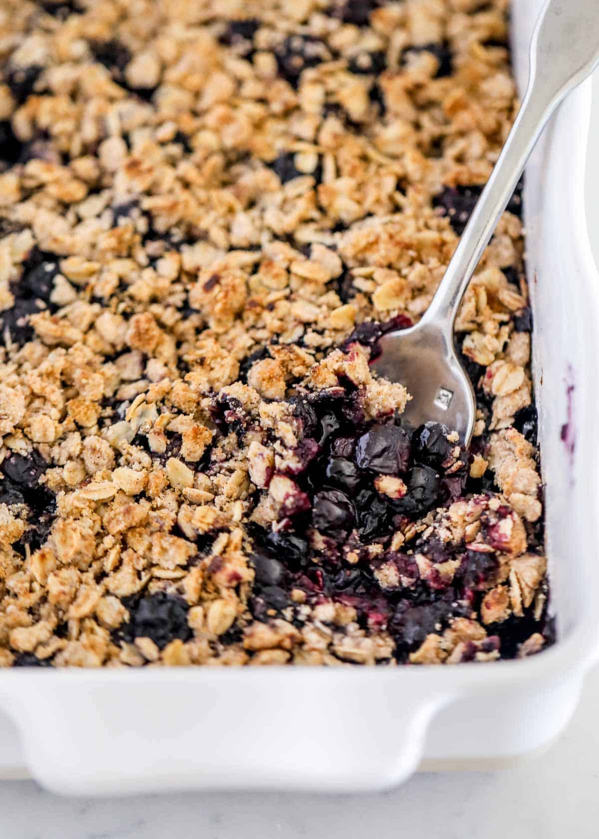 Blueberry crisp in white baking dish with spoon. 