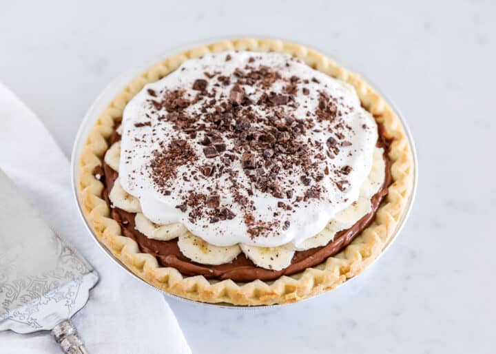 Chocolate banana cream pie is a chilled, creamy no-bake dessert that comes together in just 10 minutes! A crispy pie crust is filled with delightful chocolate and whipped cream then topped with a layer of bananas and even more whipped cream! chocolate banana cream pie on counter