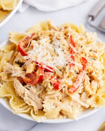 Creamy chicken pasta made with shredded chicken, peppers and onion on a white plate.