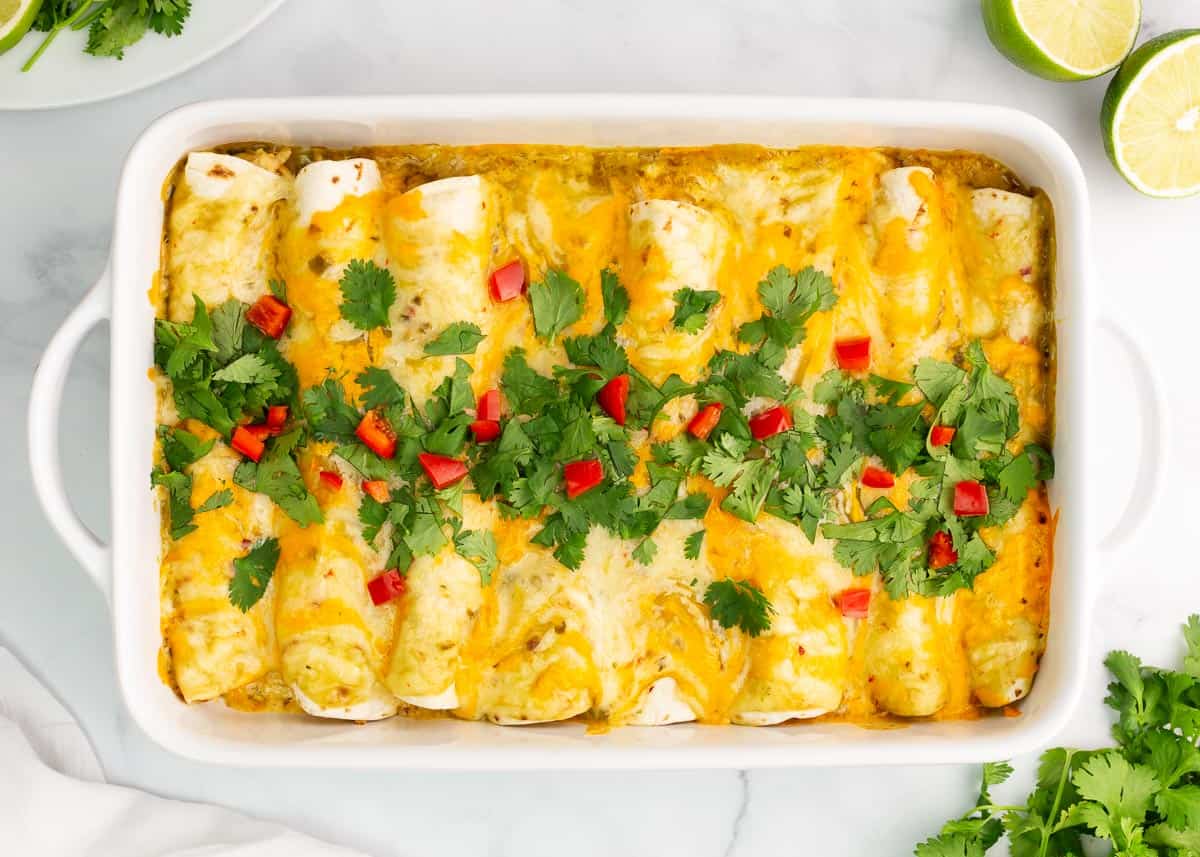 These green chile chicken enchiladas are creamy, cheesy and full of flavor! This recipe is absolutely to die for...better than a Mexican restaurant! Green chile chicken enchiladas in pan.