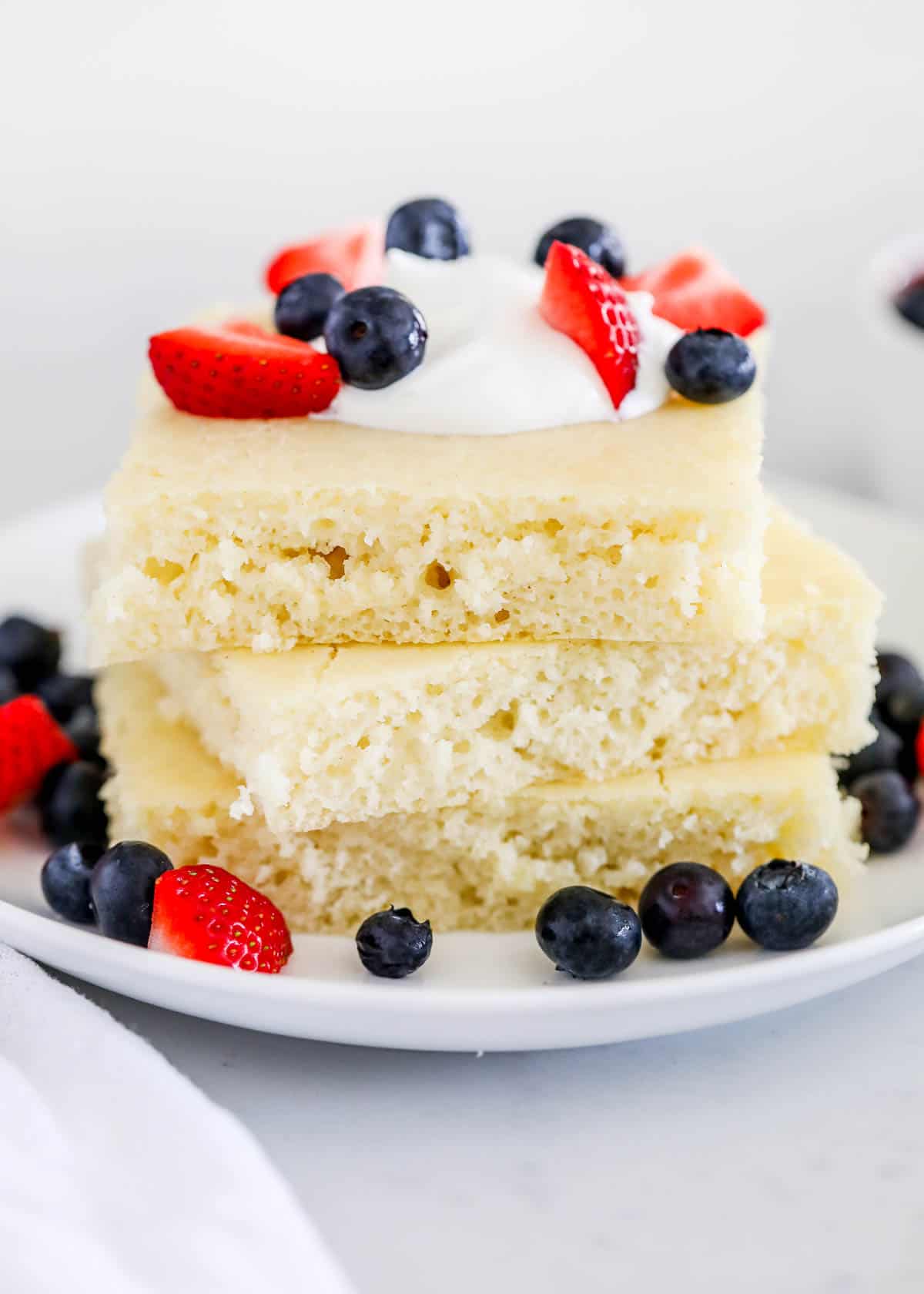 A stack of sheet pan pancakes topped with berries and whipped cream.
