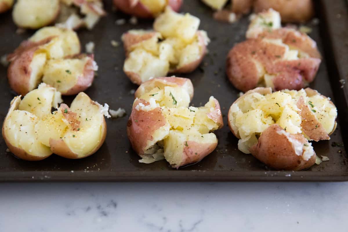 Smashed potatoes on a baking sheet with seasonings.