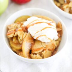 Easy apple cobbler topped with whipped cream and caramel sauce in a white bowl.