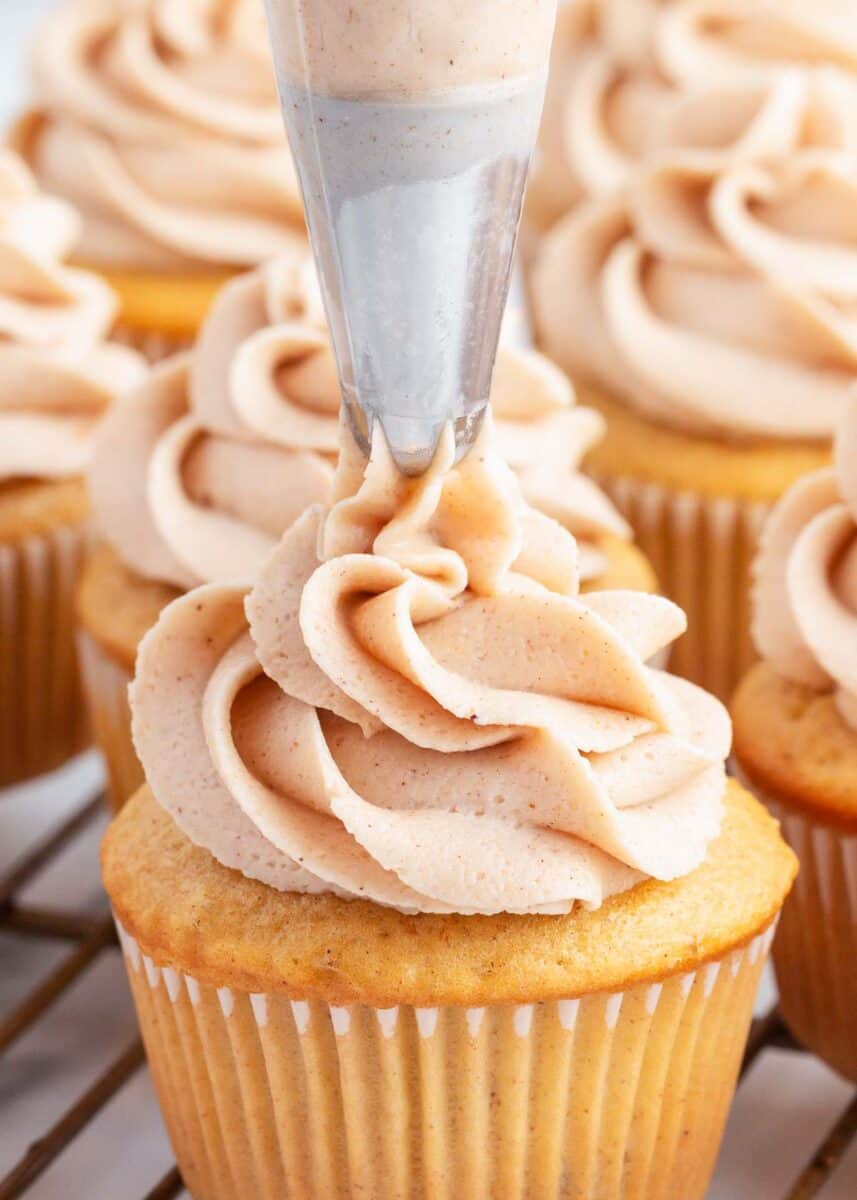 piping cinnamon frosting on apple pie cupcake