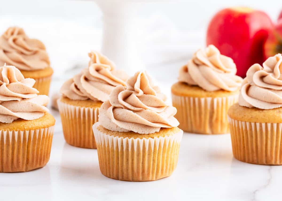 Moist and fluffy cupcakes stuffed with a sweet apple filling and then topped with cinnamon buttercream. These apple pie cupcakes are the perfect fall dessert to try this season! apple pie cupcakes on counter
