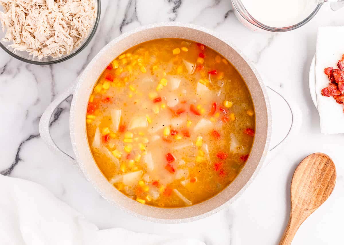Adding veggies, potatoes and broth to a pot on the stove for chicken corn chowder with potatoes.