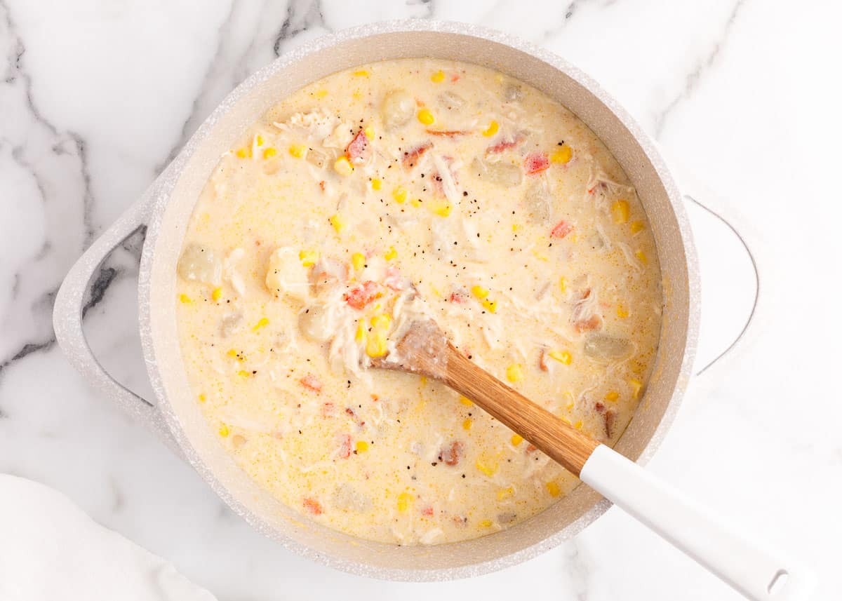 Cream added to chicken and corn chowder in a pot.