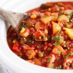 Slow cooker chicken vegetable soup in the base of the crockpot with a serving spoon.