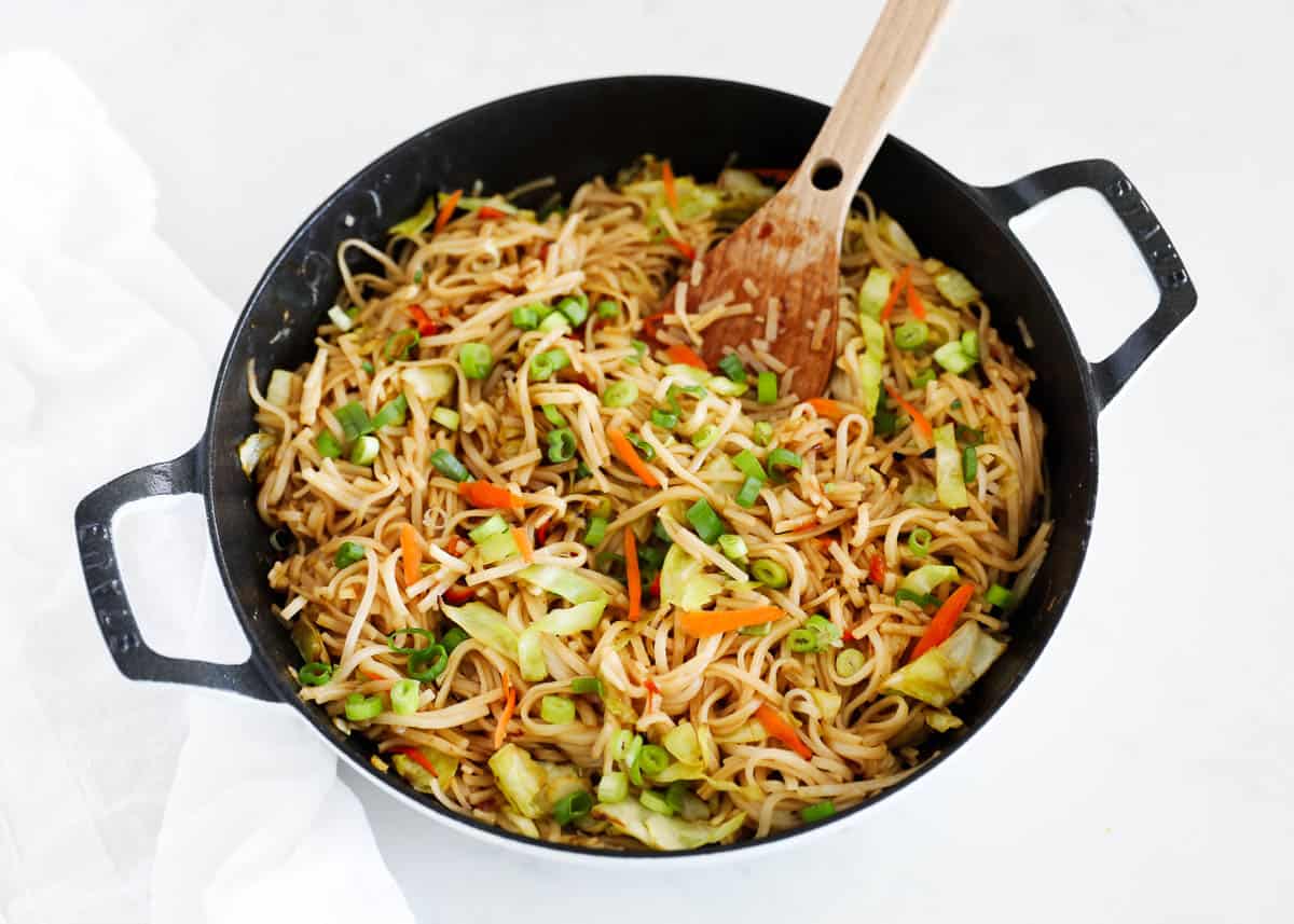 Chow mein noodles in a skillet with a wooden serving spoon.