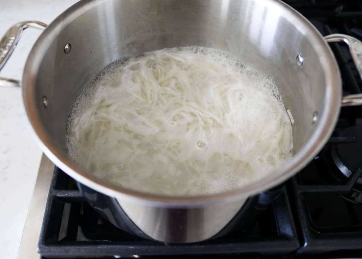 Rice noodles cooking a pot on the stove.