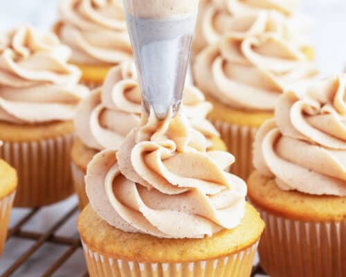 piping cinnamon buttercream onto cupcakes