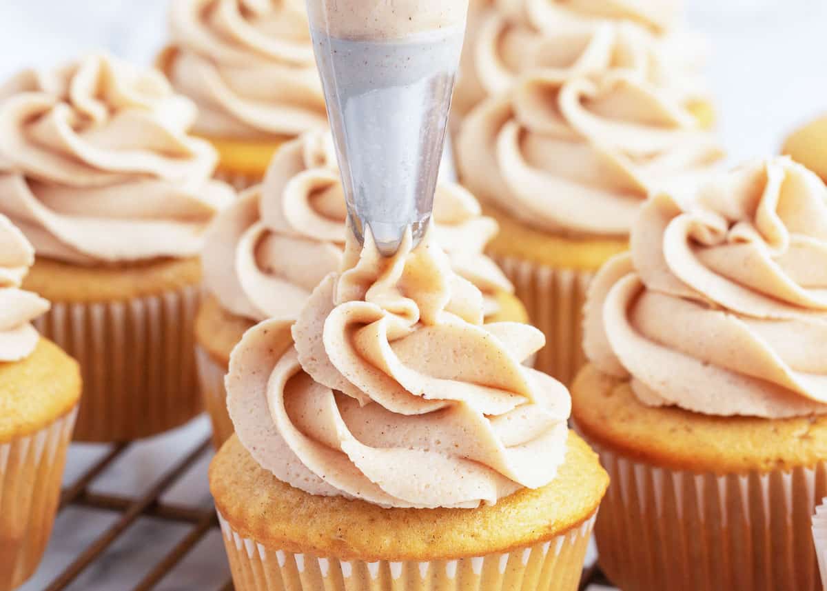 piping cinnamon buttercream onto cupcakes