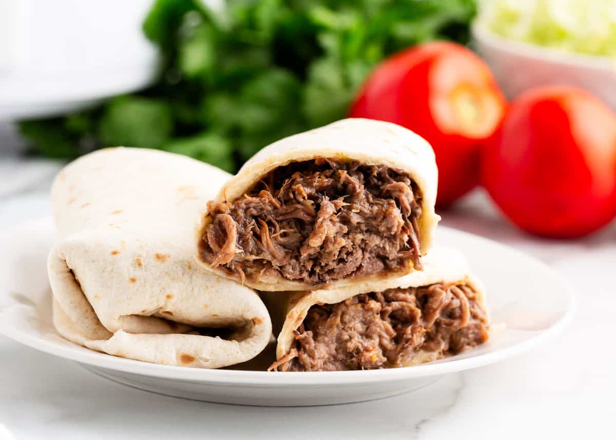 Warm flour tortillas filled with tender slow cooker shredded beef and finished off with your favorite toppings. These green chili burritos are delicious, easy, and perfect for a weeknight dinner for busy families! green chili burritos on white plate