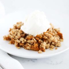 Pumpkin crisp with a scoop of vanilla ice cream on a white plate.