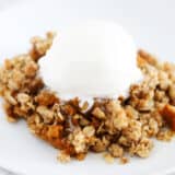 A serving of pumpkin crisp with a scoop of vanilla ice cream on a white plate.