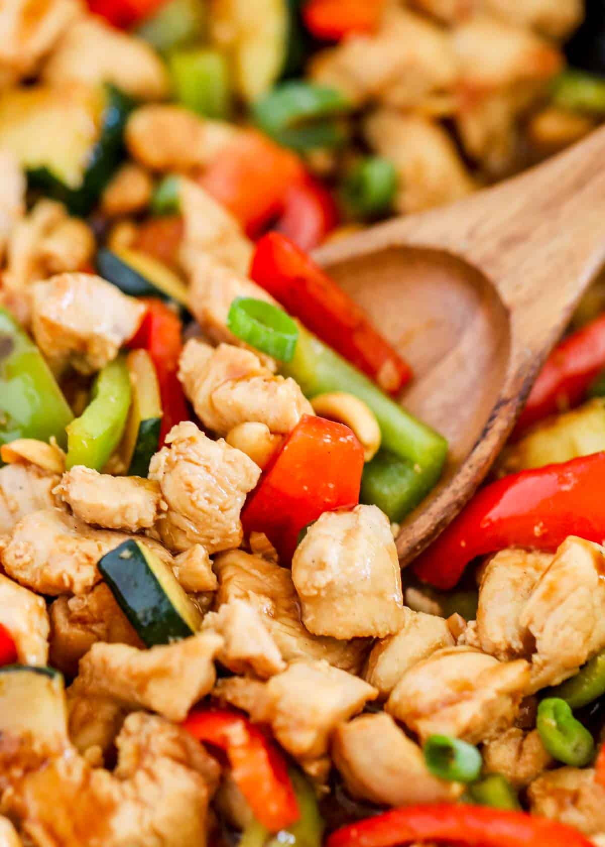 Kung Pao chicken in a skillet with wooden spoon.