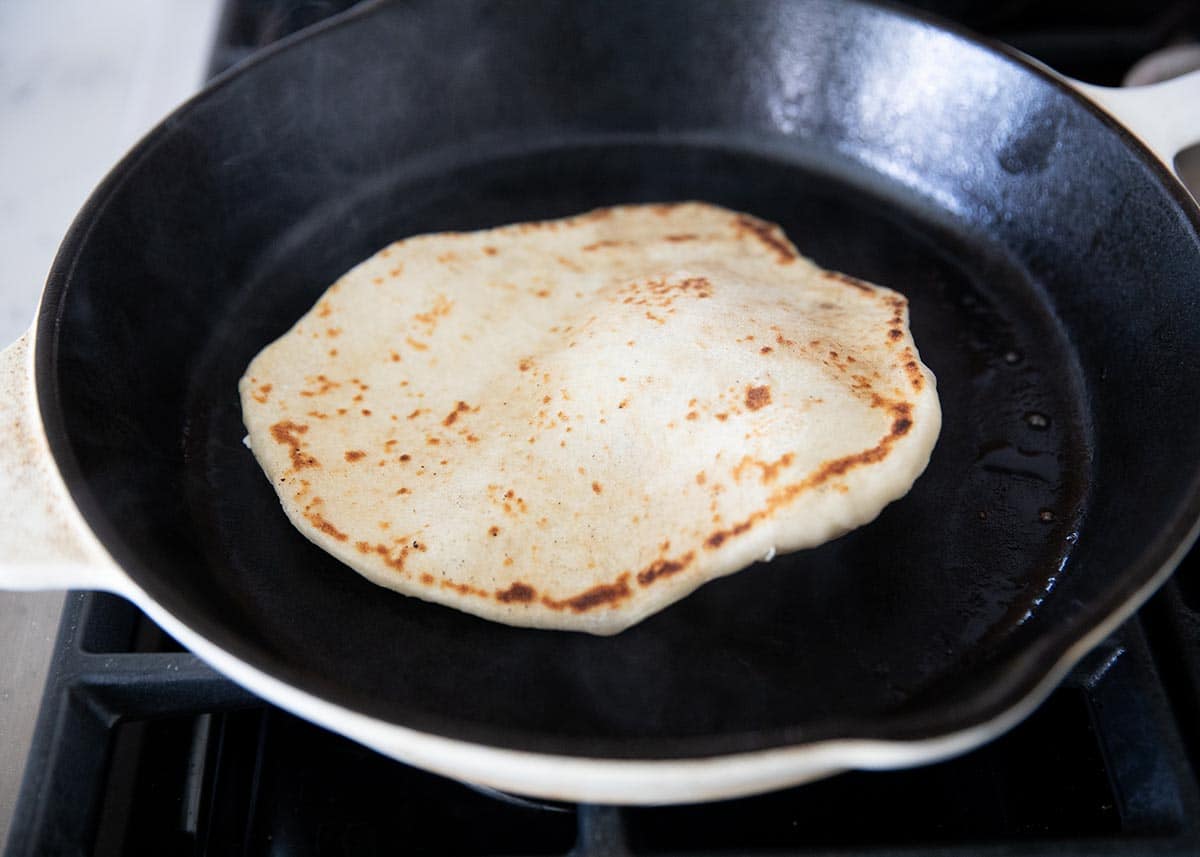 Naan bread cooking in a hot skillet until golden and lightly charred.