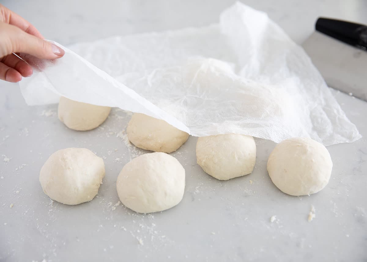 Portioned naan dough balls resting on the counter covered with a kitchen towel.