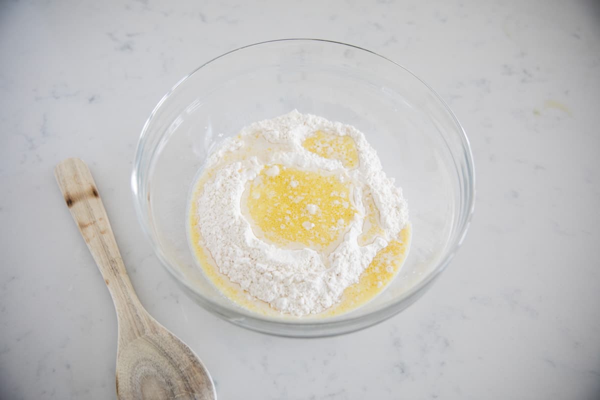Flour with yogurt, oil, and yeast added in a mixing bowl to make homemade naan dough.