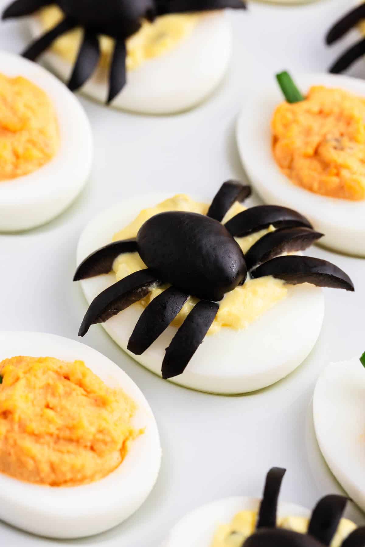 Halloween deviled egg spiders and pumpkins on white plate.