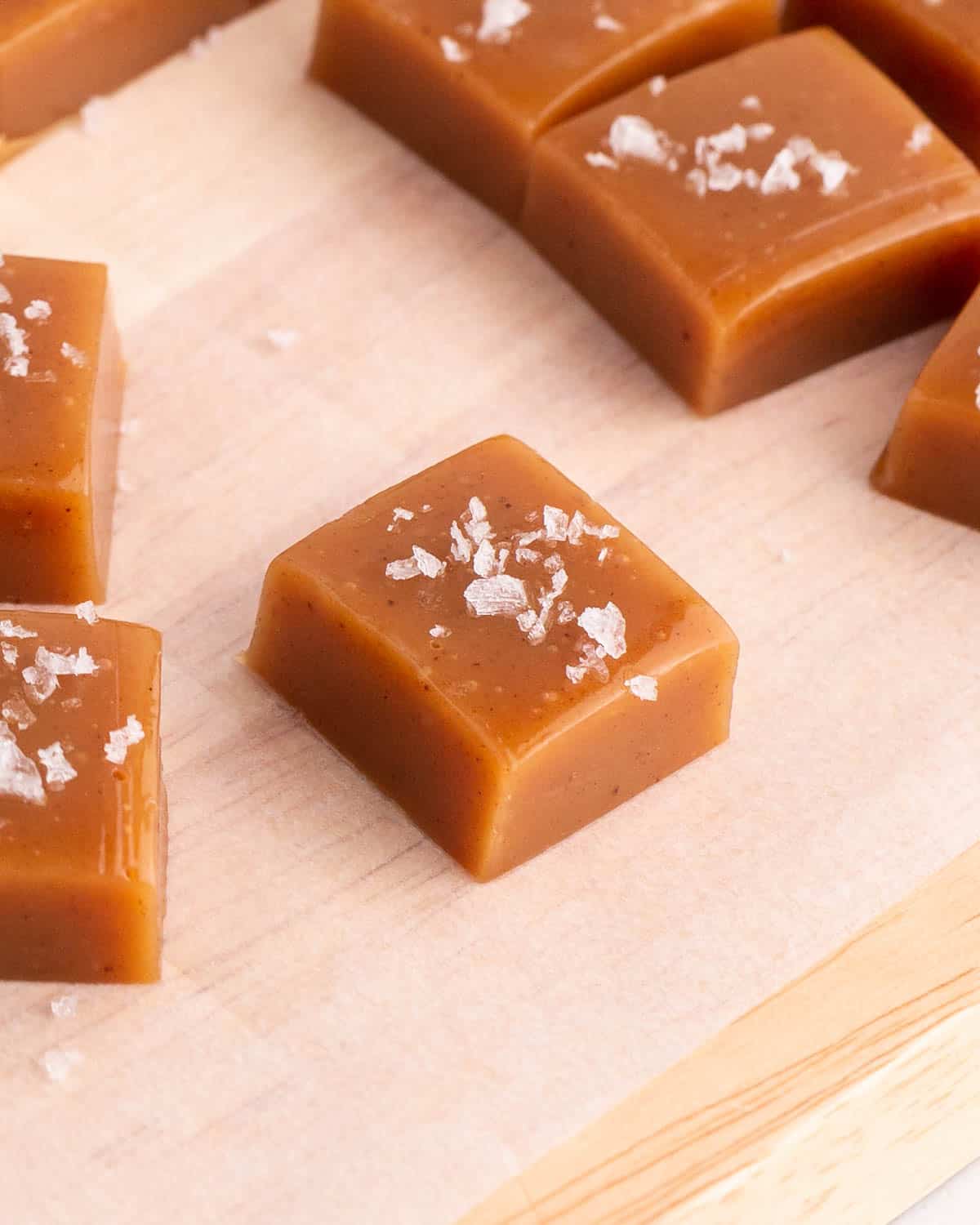Apple cider caramels arranged neatly on parchment paper, each topped with a light sprinkle of sea salt.