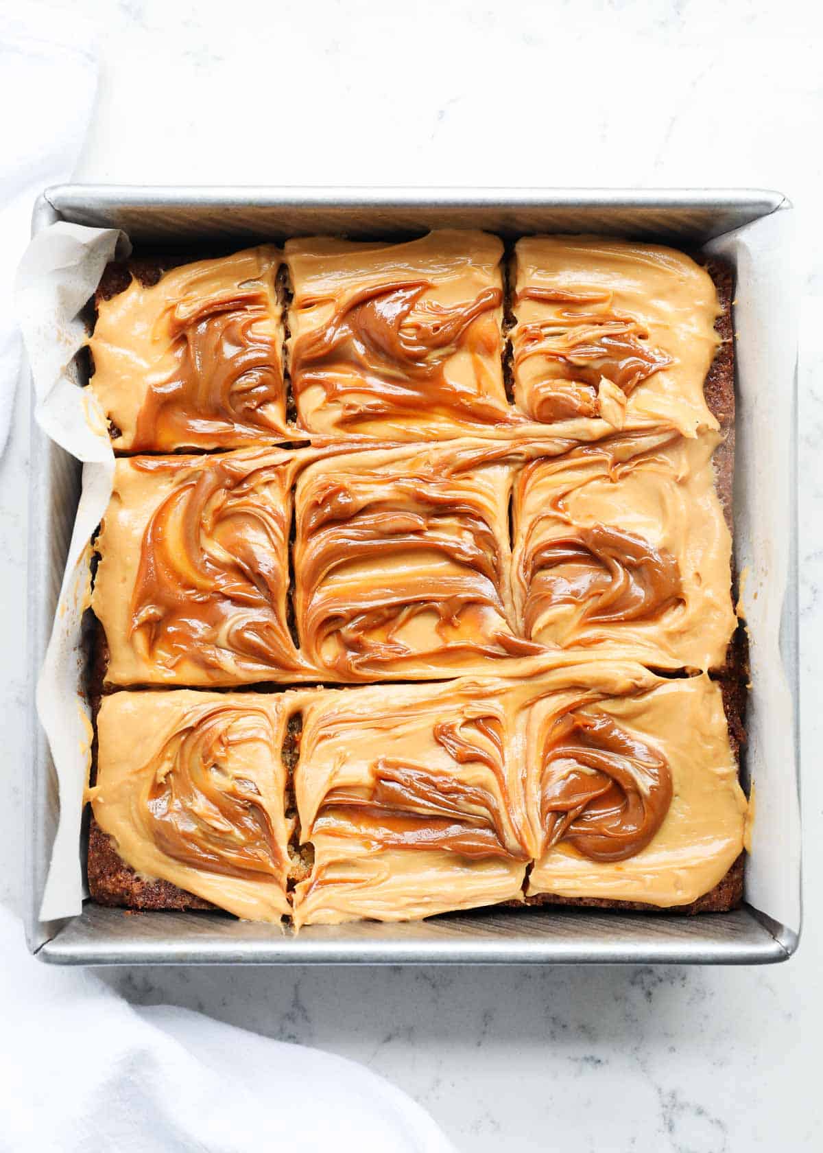 A cake in a pan frosted with caramel cream cheese frosting and cut into squares.