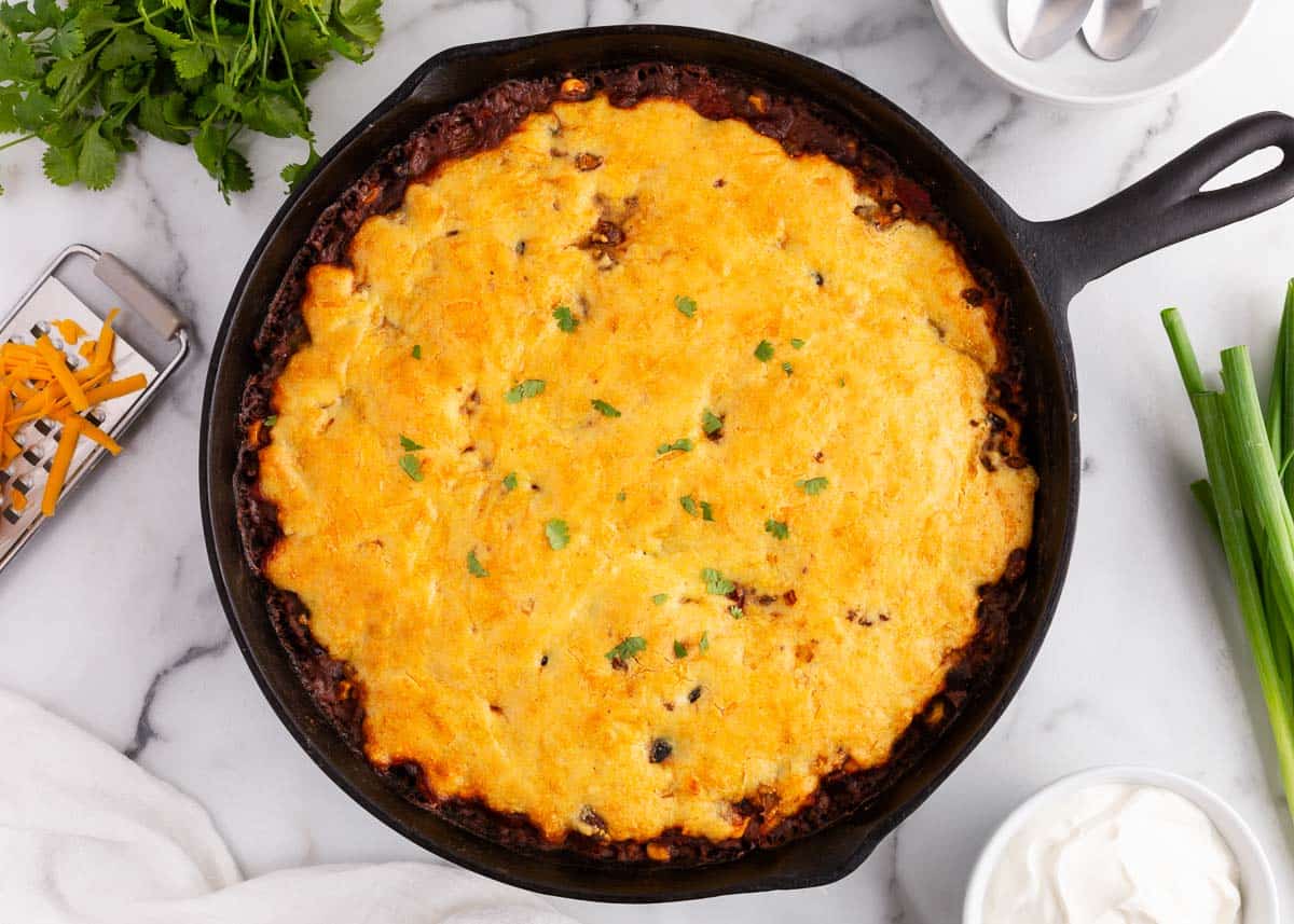 This chili and cornbread skillet is a comforting and flavorful dish made all in one pan. The cornbread is cooked right on top of the chili, adding a hearty layer of deliciousness! chili cornbread skillet on counter