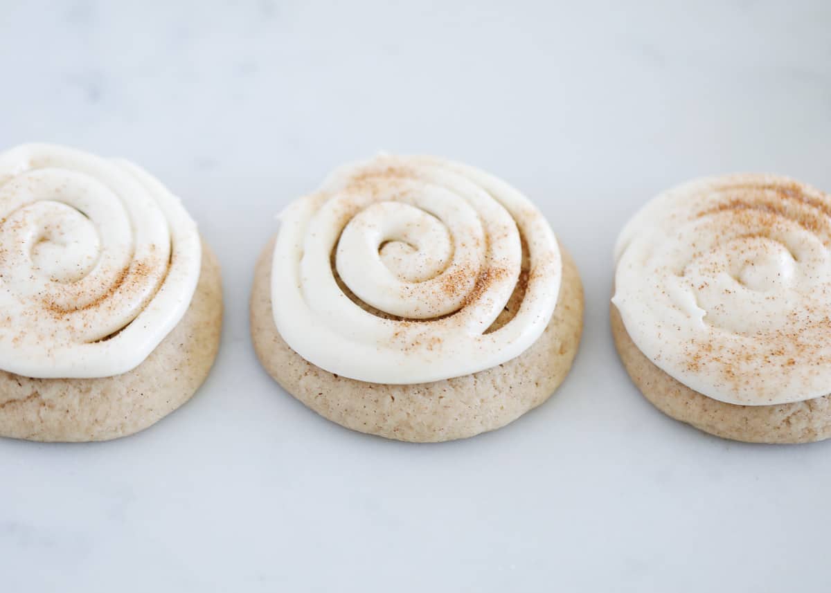 This recipe for cinnamon roll sugar cookies is simple to make and will have you looking like a total baking rock star. You won't believe how delicious these cookies are! Frosted cinnamon roll cookies on counter.
