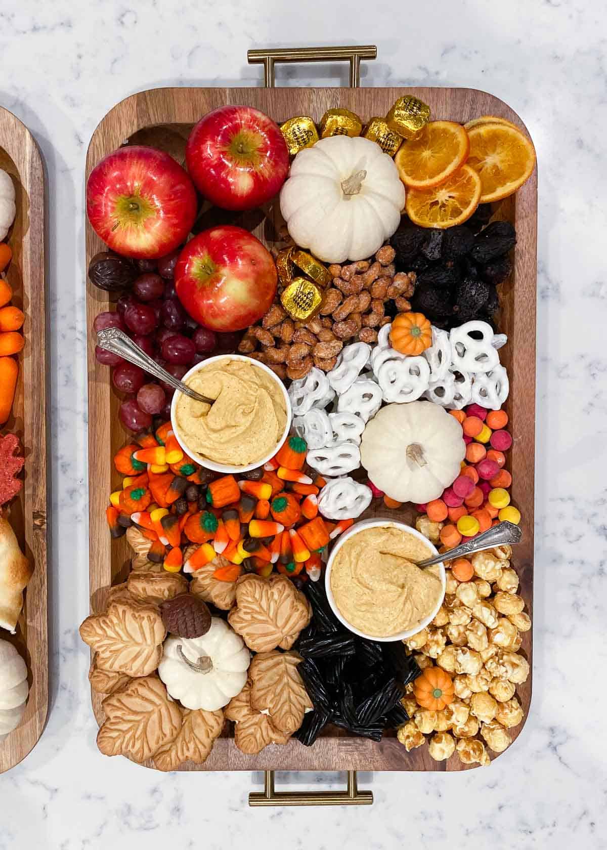 Fall charcuterie board on counter with bowls of pumpkin cheesecake dip, pretzels, apples, cookies and candy.