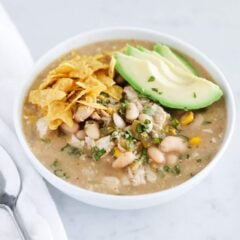 Crock pot green enchilada chicken soup in bowl topped with avocado, cilantro and tortilla strips.
