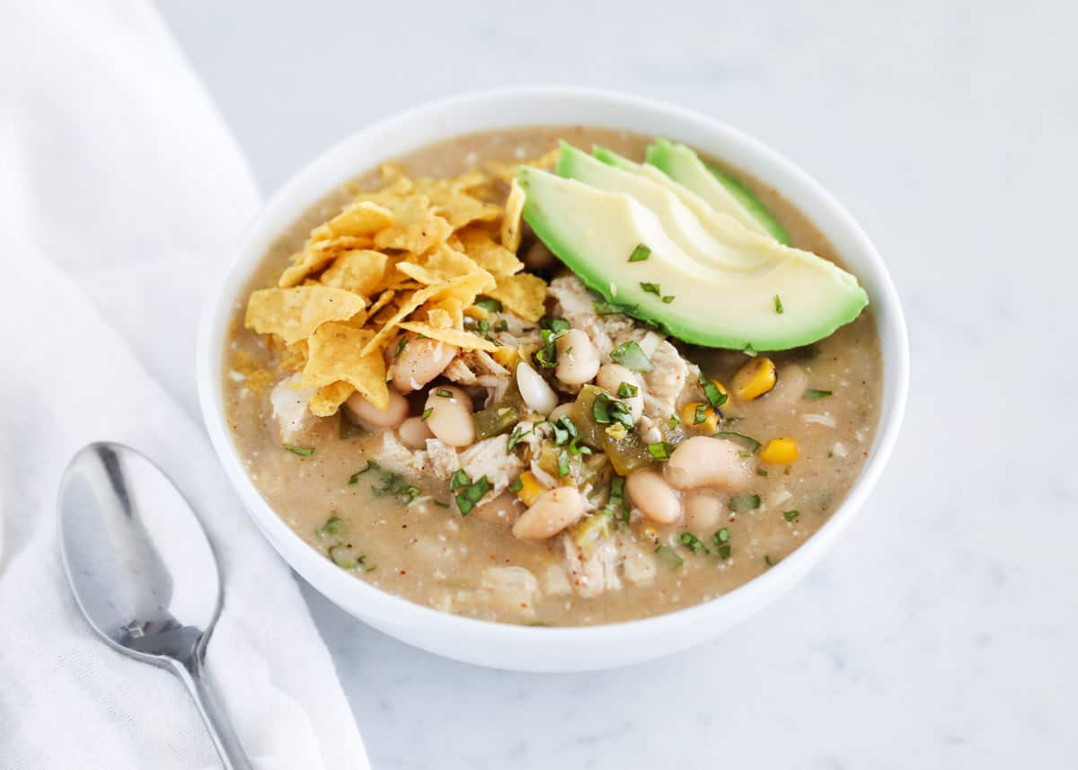 This slow cooker green enchilada soup has everything you love about the classic green chile chicken enchiladas in the form of soup. It only takes about 10 minutes to prep and then the crockpot does all the rest! Green enchilada chicken soup in bowl with garnish of avocado and tortilla strips.