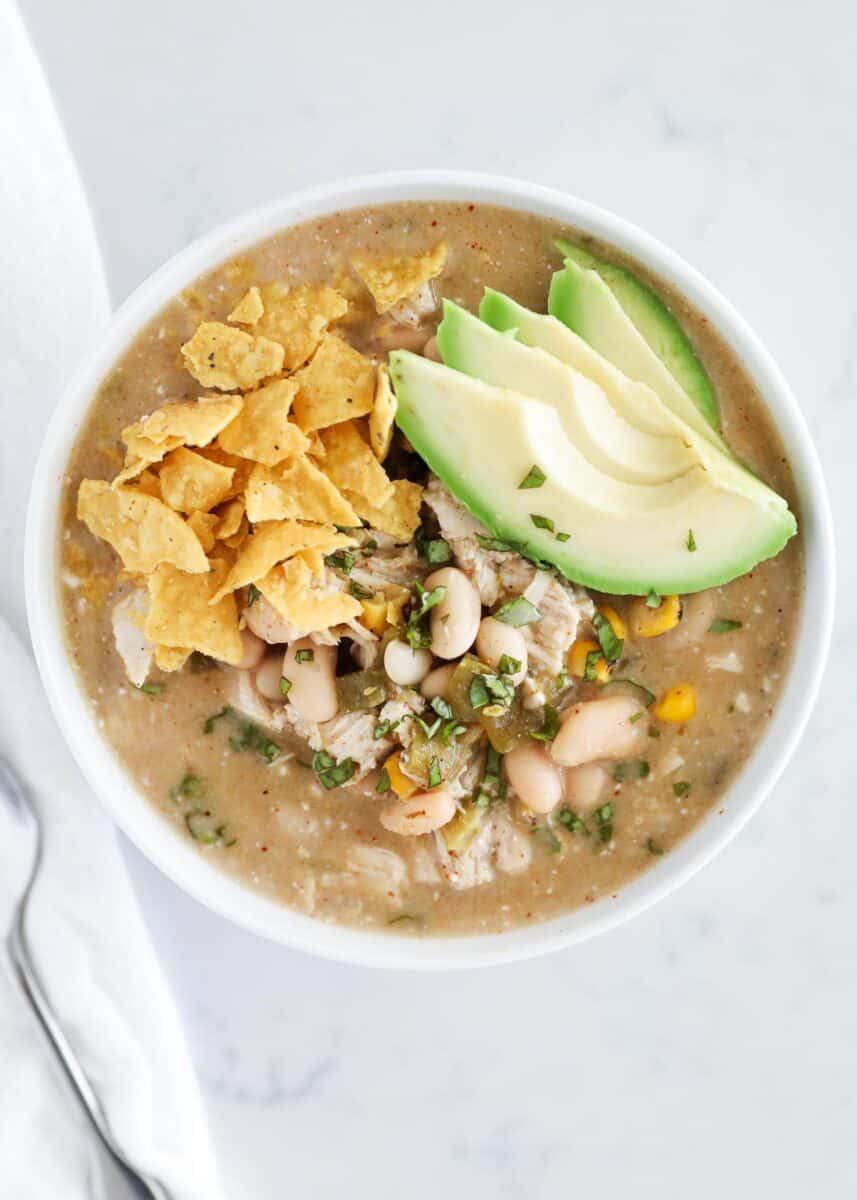 Green enchilada chicken soup in bowl with avocado and crushed tortillas.