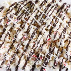Peppermint bark popcorn drizzled with chocolate on a parchment lined baking sheet.