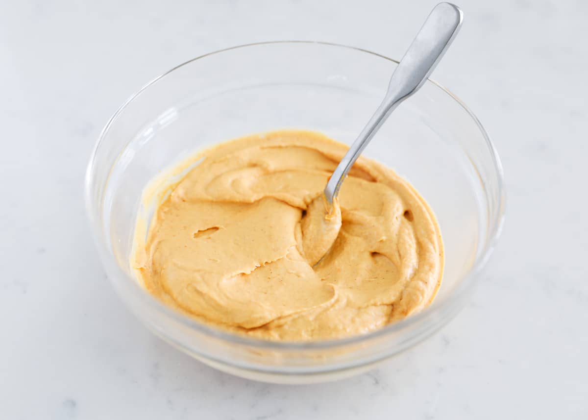 Mixing pumpkin cream cheese dip in glass bowl.