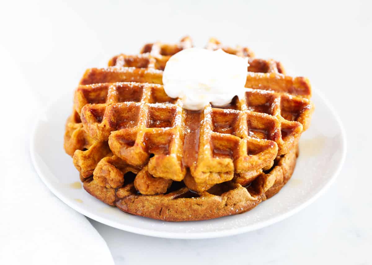 Two pumpkin waffles stacked on a white plate with butter and syrup.