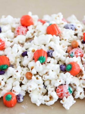 Halloween popcorn coating in white chocolate and mixed with Halloween candy on parchment paper.