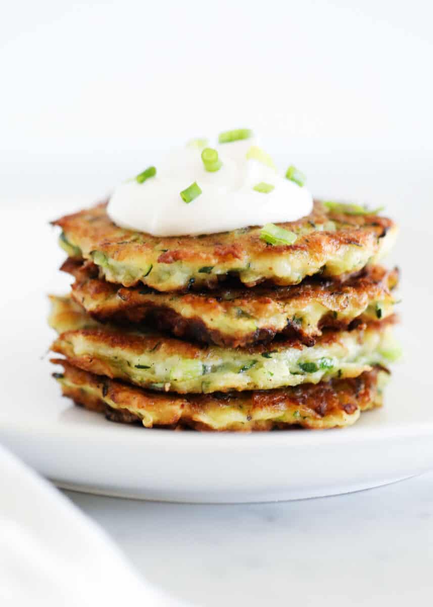 Stack of zucchini fritters with sour cream.