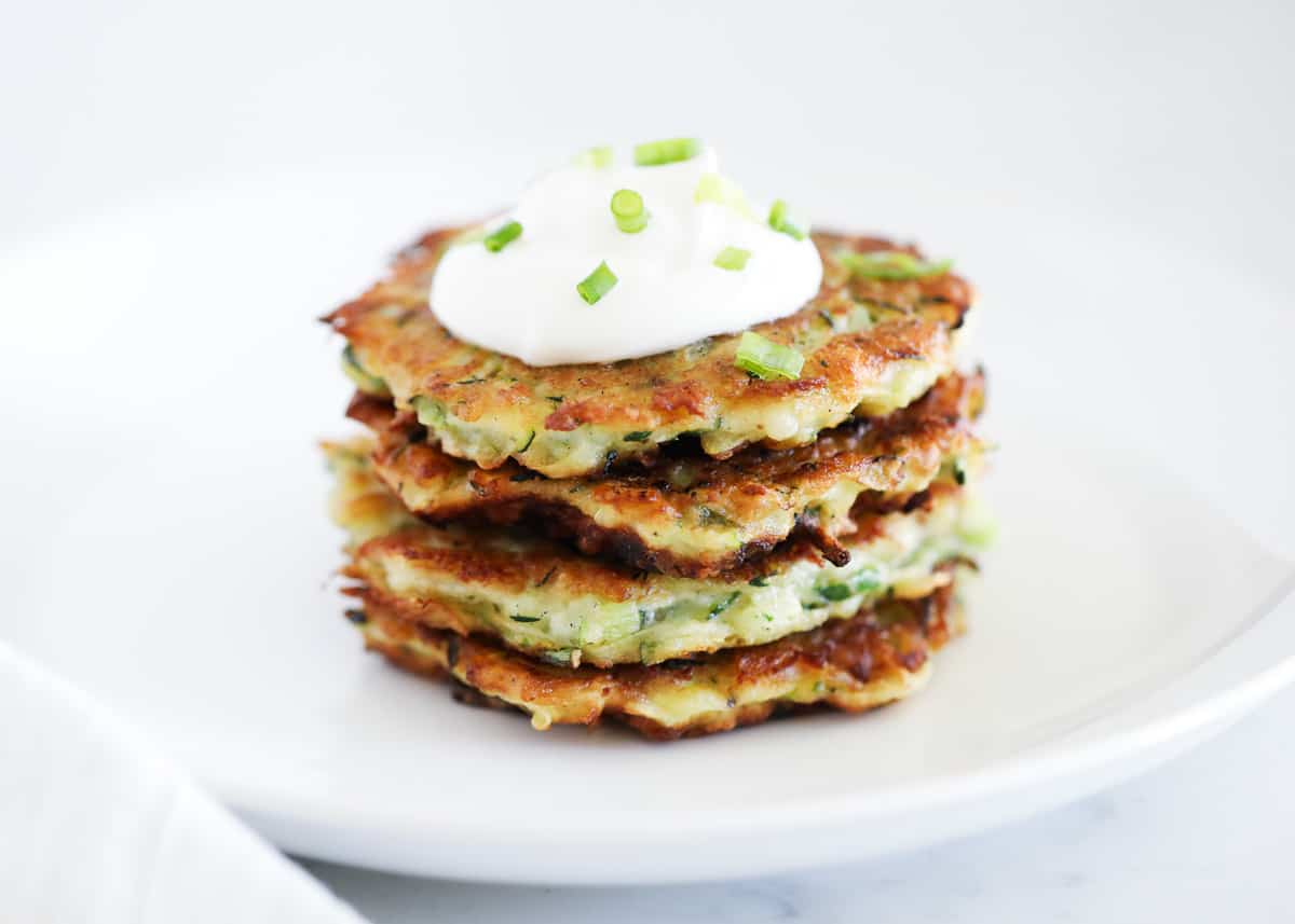 Stack of zucchini fritters on white plate.