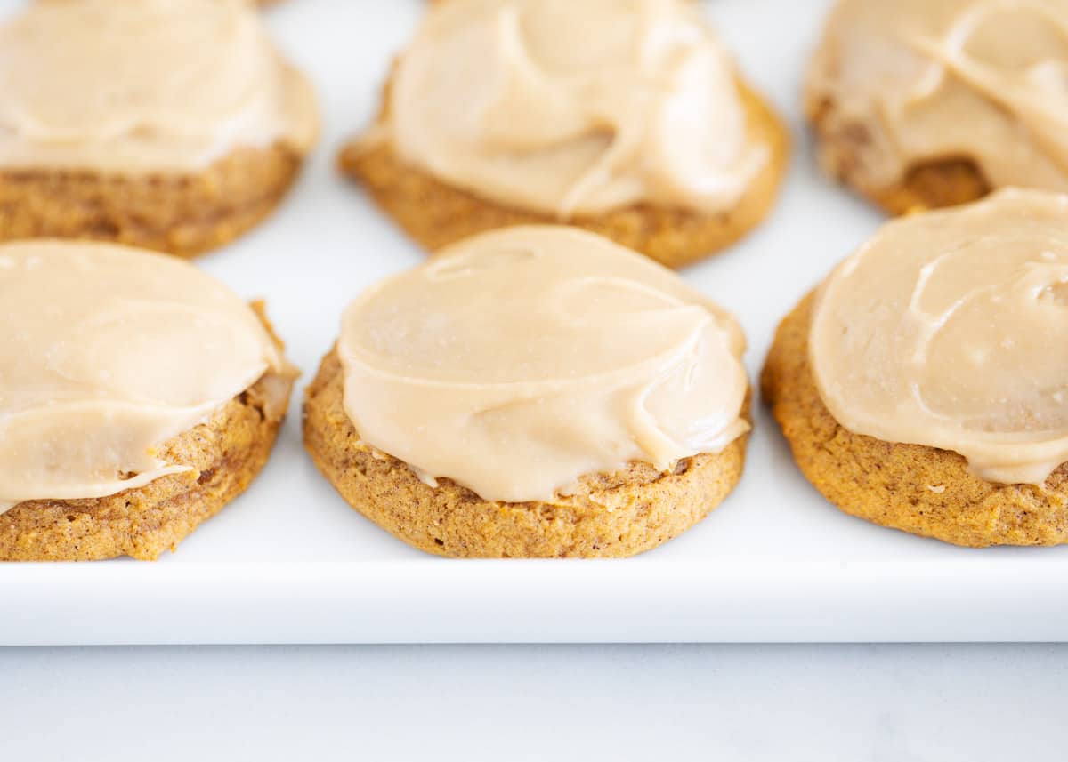 Melt in your mouth soft pumpkin cookies topped with rich caramel icing. Simply the best pumpkin dessert out there and a must-make this fall! Pumpkin cookies on white plate.