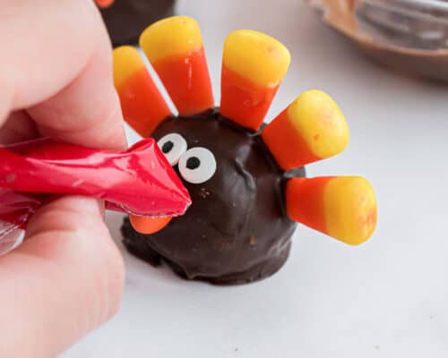 using bag with red frosting to draw beak on turkey oreo ball