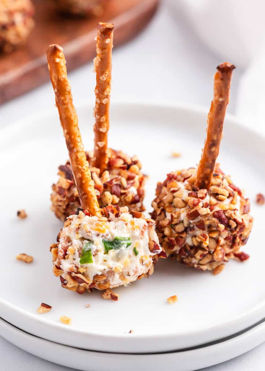 Cheese ball bites are flavorful appetizers that are perfect for snacking or serving at parties. These mini cheese balls are loaded with everyone's favorite ingredients, and they are incredibly simple to make. cheese ball bites on white plates