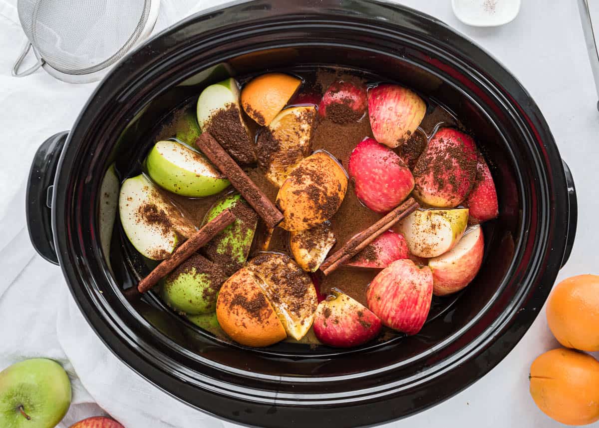 Orange, apples and cinnamon placed in crock pot for apple cider.