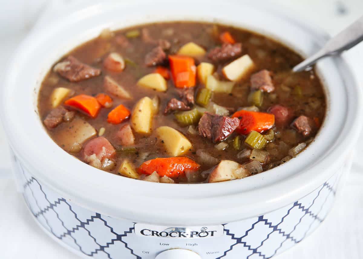 Crockpot beef stew in a slow cooker with a soup ladle.