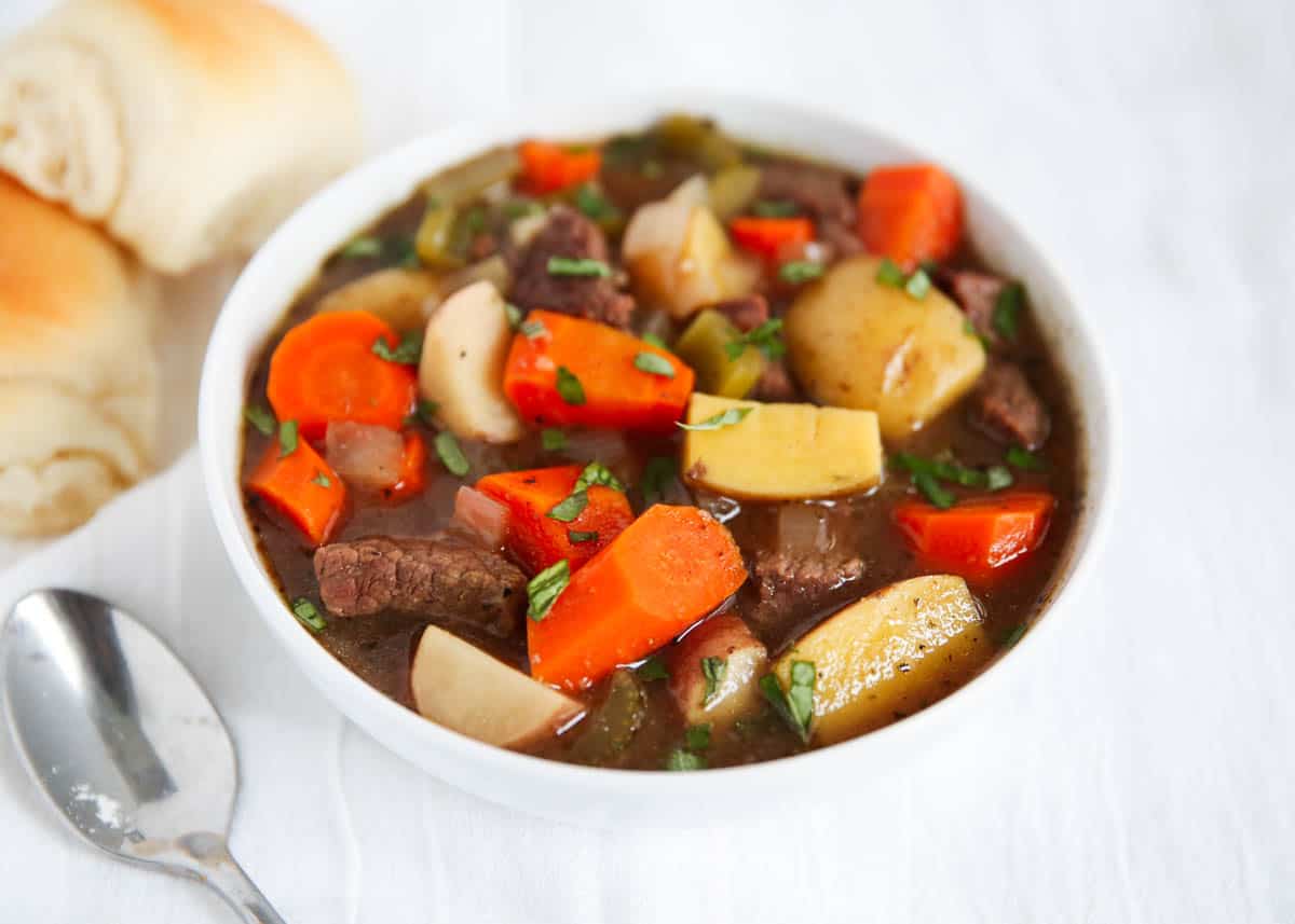 beef stew in white bowl with rolls