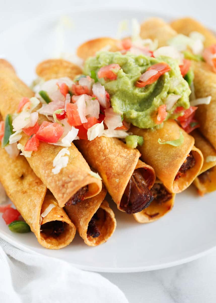 Easy to make beef taquitos with a crispy corn tortilla shell filled with seasoned shredded beef and melty cheese. Top with pico de gallo and guacamole, and a side of sour cream for dipping! beef taquitos with guacamole and pico on top