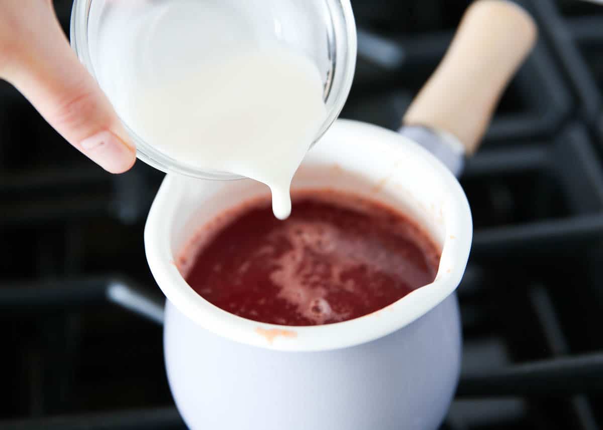 Pouring cornstarch slurry into a pot with sweet and sour sauce.
