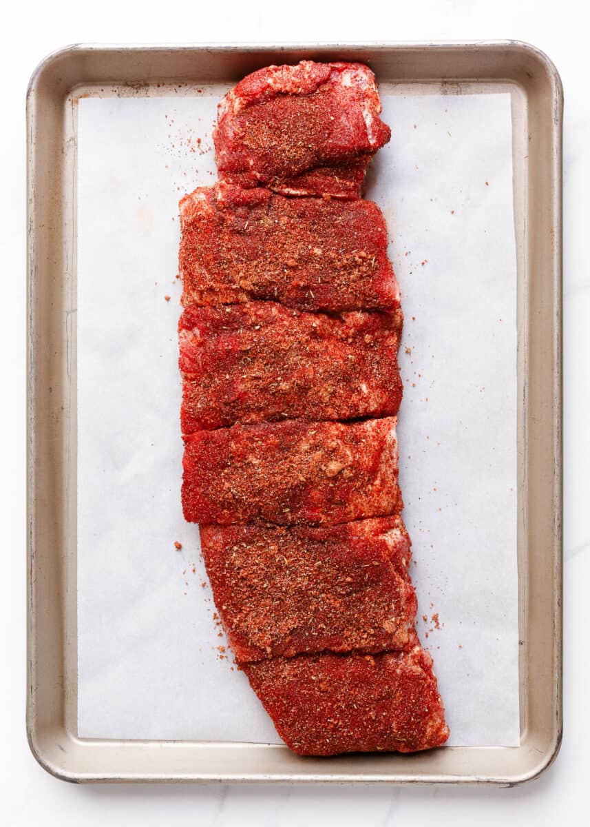Slow Cooker Ribs - Easy baby back ribs smothered with a homemade rub and sweet and tangy barbecue sauce. Cooked to perfection in the crockpot and fall off the bone delicious. These are the best slow cooker ribs! ribs on sheet pan with a rub